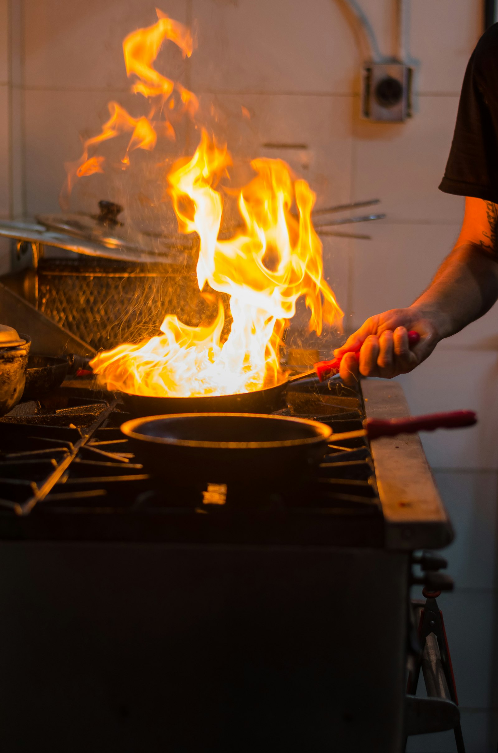 A chef working a flaming pan in a dark kitchen