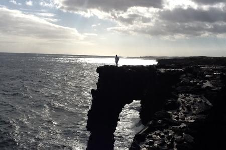 A figure standing on a sea cliff arch at dusk
